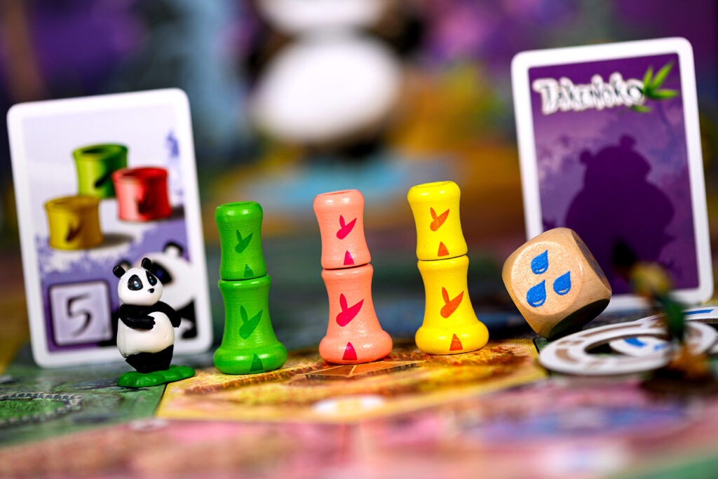 Close-up van drie speelstukken, één dobbelsteen en twee spelkaarten van Takenoko