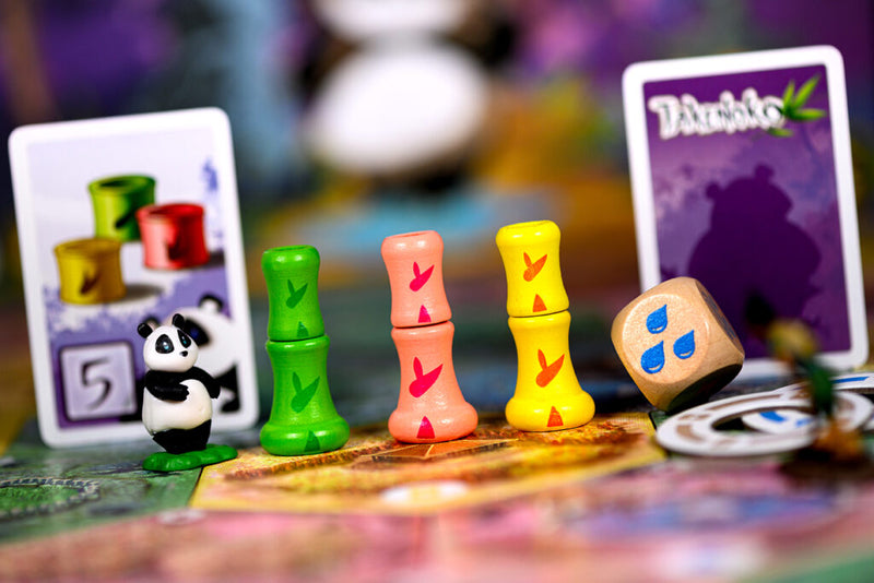 Close-up van drie speelstukken, één dobbelsteen en twee spelkaarten van Takenoko